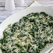 Fried spinach with fresh shredded cheese on top in a serving dish ready to serve.