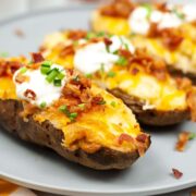 Twice baked potatoes on a plate topped with bacon pieces and sour cream ready to serve.