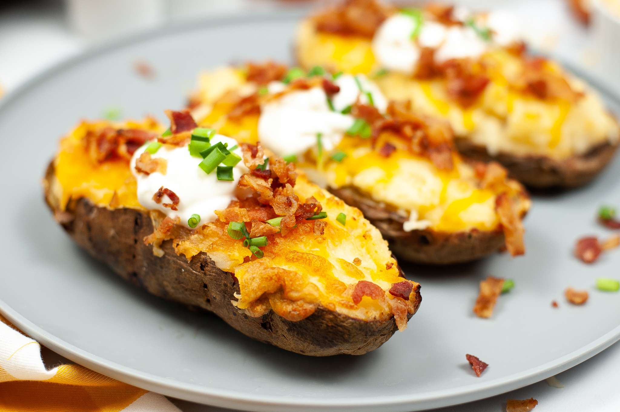 Twice baked potatoes on a plate topped with bacon pieces and sour cream ready to serve.