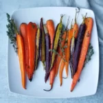 Roasted rainbow carrots sliced in half on a plate with thyme as a garnish.