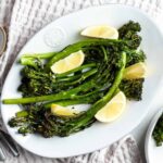 Cooked broccolini on a serving plate with lime wedges as a garnish.