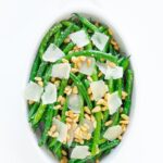 Green beans in a serving dish topped with fresh parmesan and pine nuts.