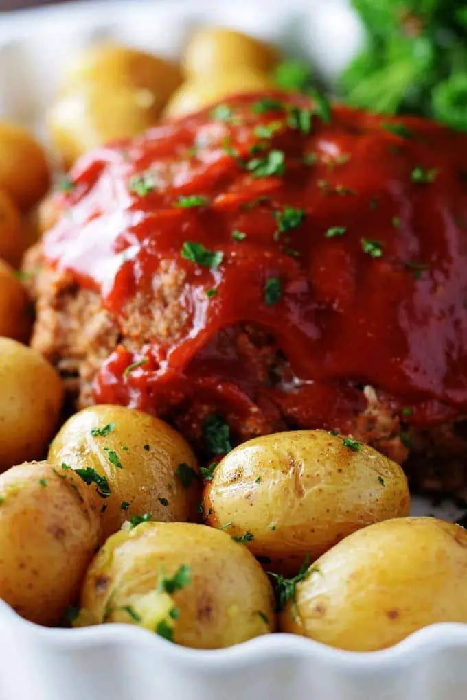 Meatloaf topped ready to cut with some baby potatoes in a serving dish ready to serve.