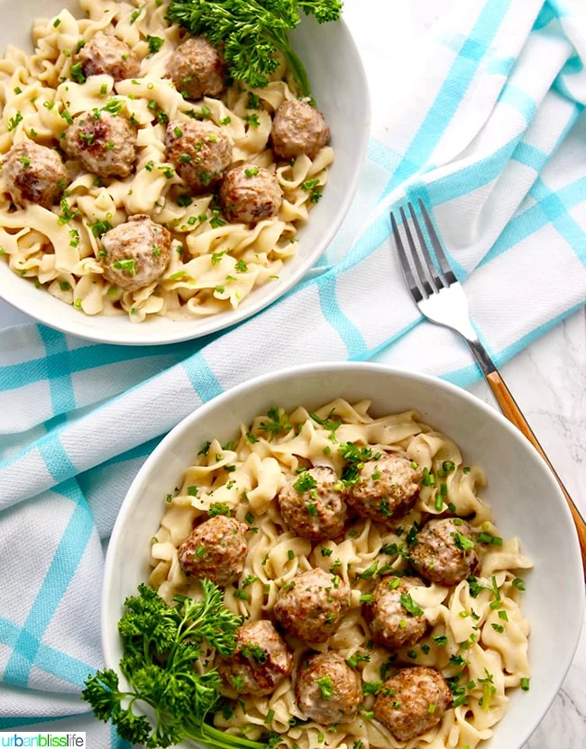 Swedish meatballs over egg noodles in a dish ready to eat garnished with fresh parsley.