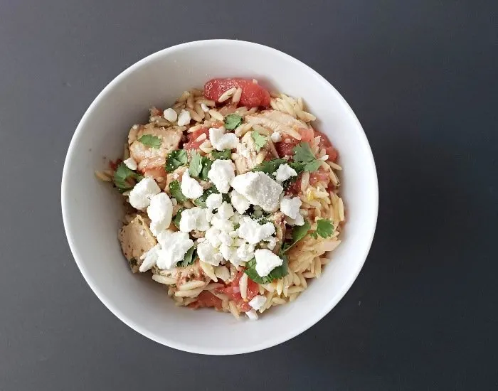 Mediterranean chicken orzo in a bowl topped with crumbled feta cheese ready to eat.