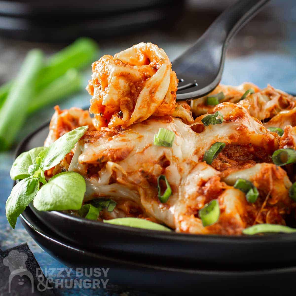 Tortellini in sauce topped with melted cheese in a serving dish with fresh herbs as a garnish.