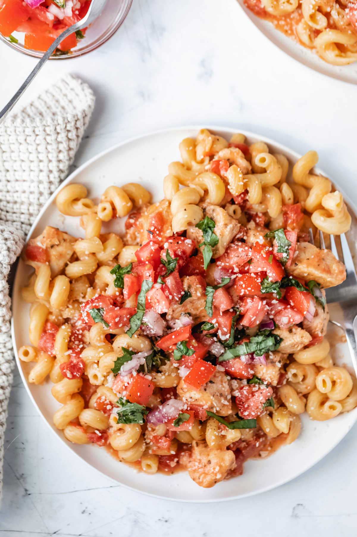 Bruschetta chicken and pasta in a dish ready to eat garnished with parmesan cheese and fresh herbs.