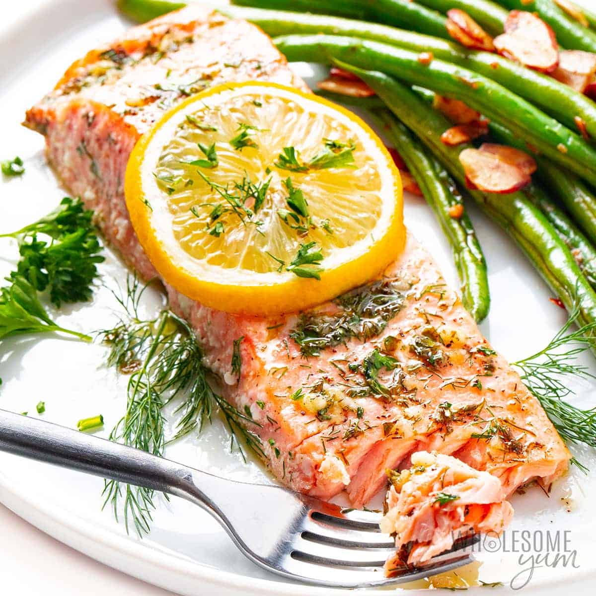 Baked salmon on a plate garnished with lemon and fresh spices.
