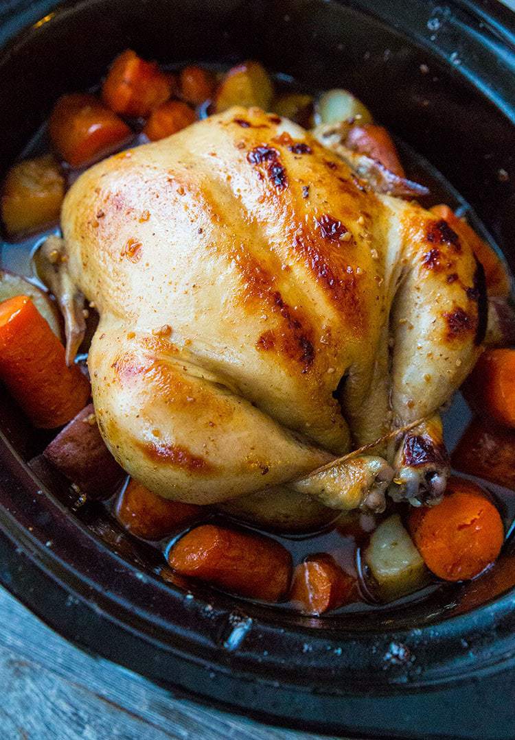 whole chicken on top of vegetables in the slow cooker after cooking before serving.