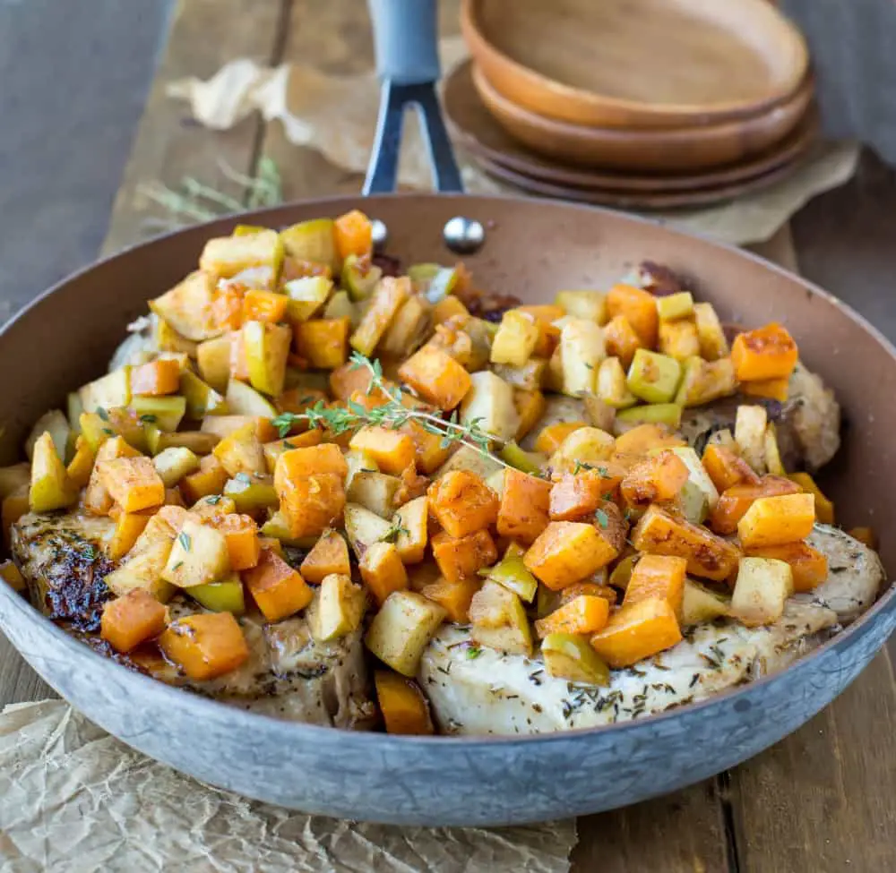 Pork chops in a frying pan topped with chopped apples and squash ready to serve.