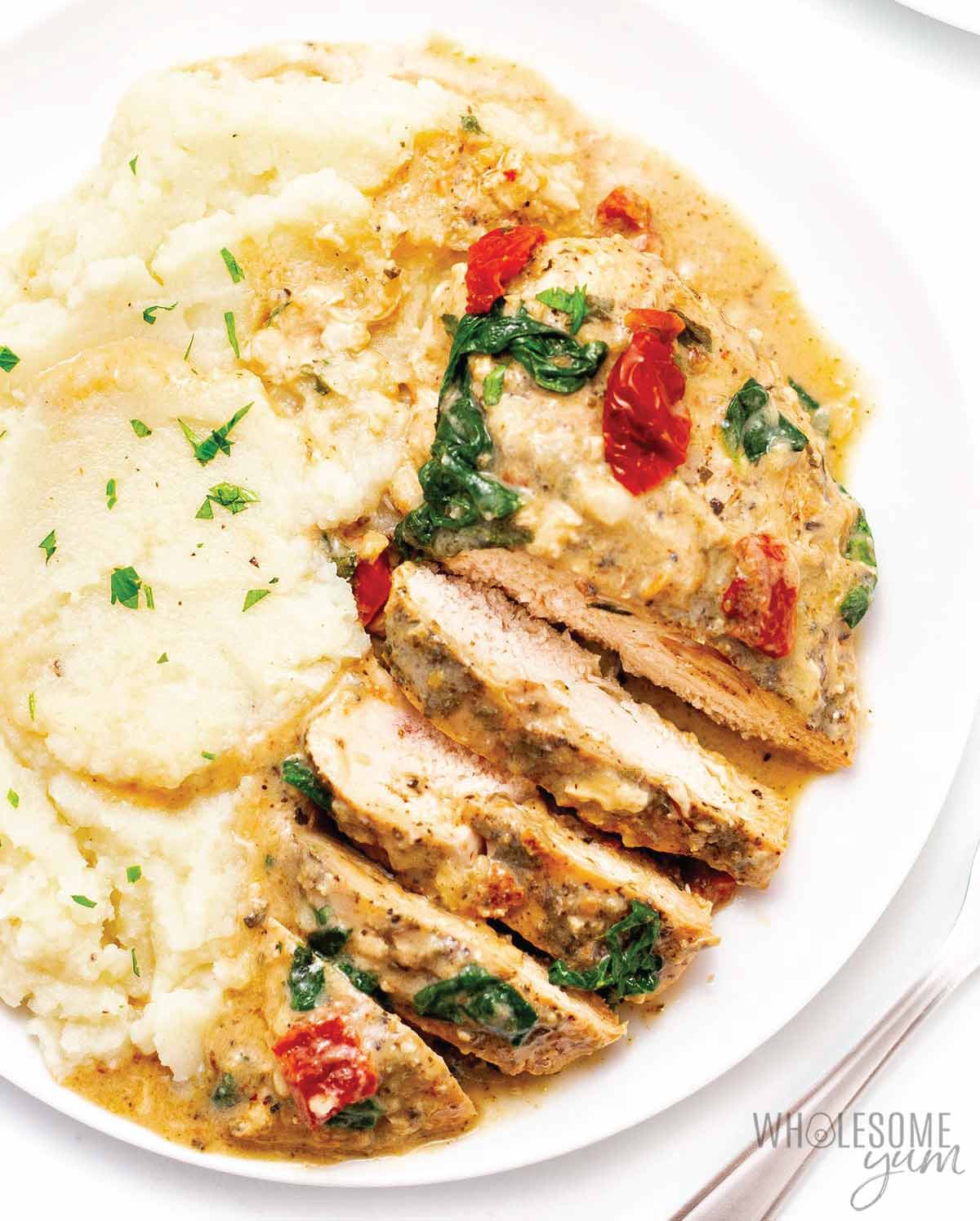 Creamy Tuscan chicken sliced on a plate served with mashed potatoes.