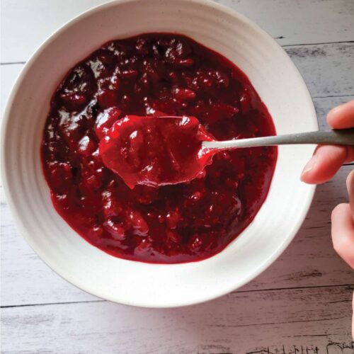 Homemade cranberry sauce in a serving bowl with a spoon scooping some out.