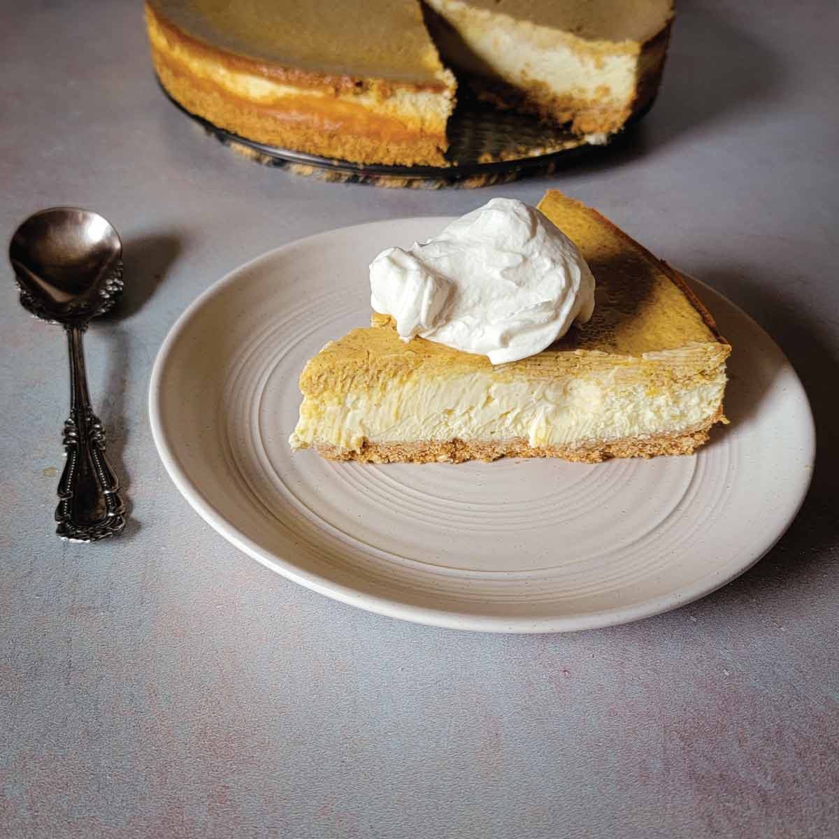 Slice of pumpkin layered cheesecake on a serving plate topped with homemade whipped cream.