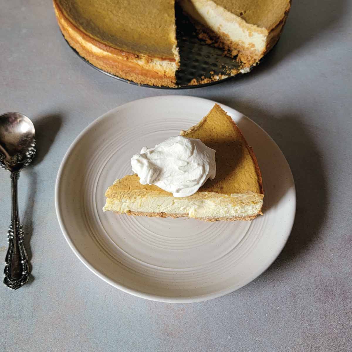 Slice of pumpkin layered cheesecake on a serving plate topped with homemade whipped cream.