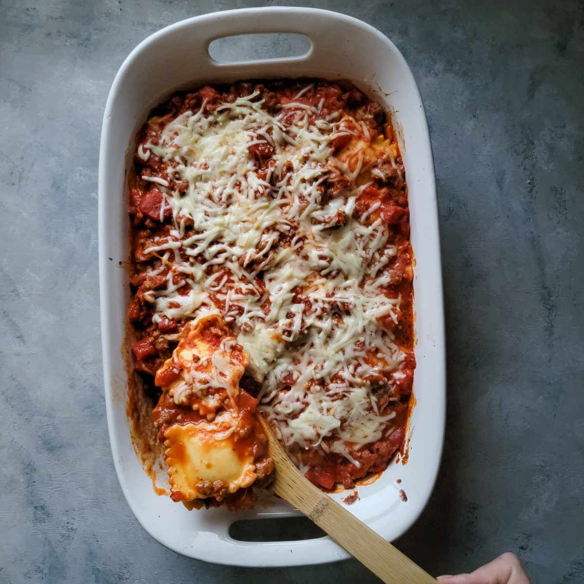 Baked ravioli being spooned out of a baking dish after cooking.