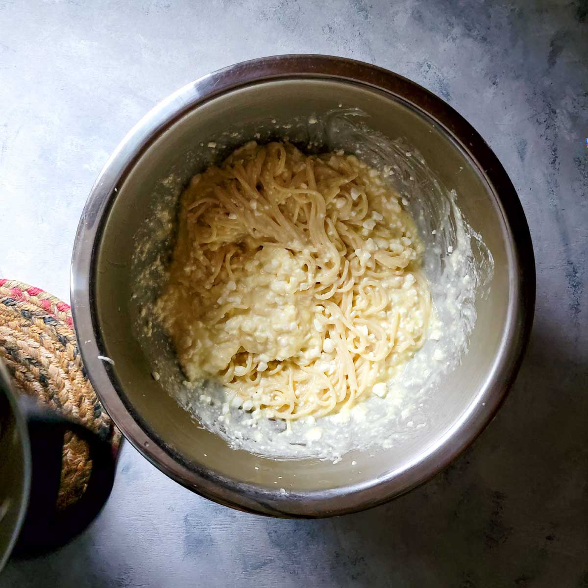 Pasta mixed with cheese, butter and egg in a bowl ready to use in layering the casserole.