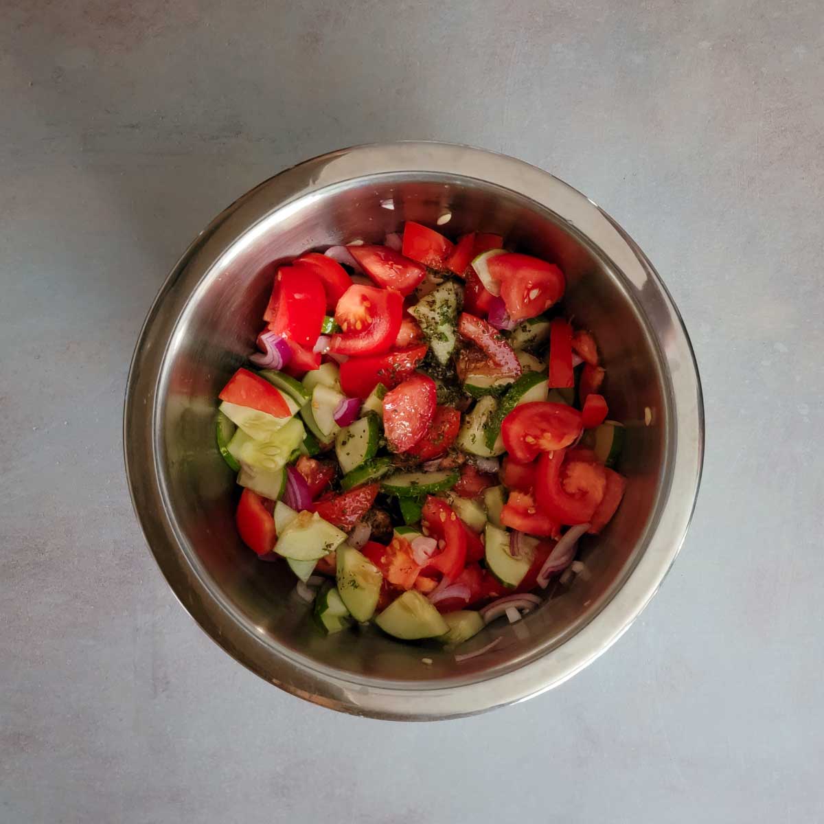 cucumbers, tomatoes and onions chopped in a mixing bowl with dressing poured over top.
