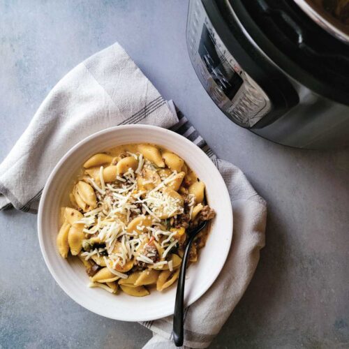 Philly cheesesteak pasta in a serving bowl with shredded cheese on top as a garnish, ready to serve.