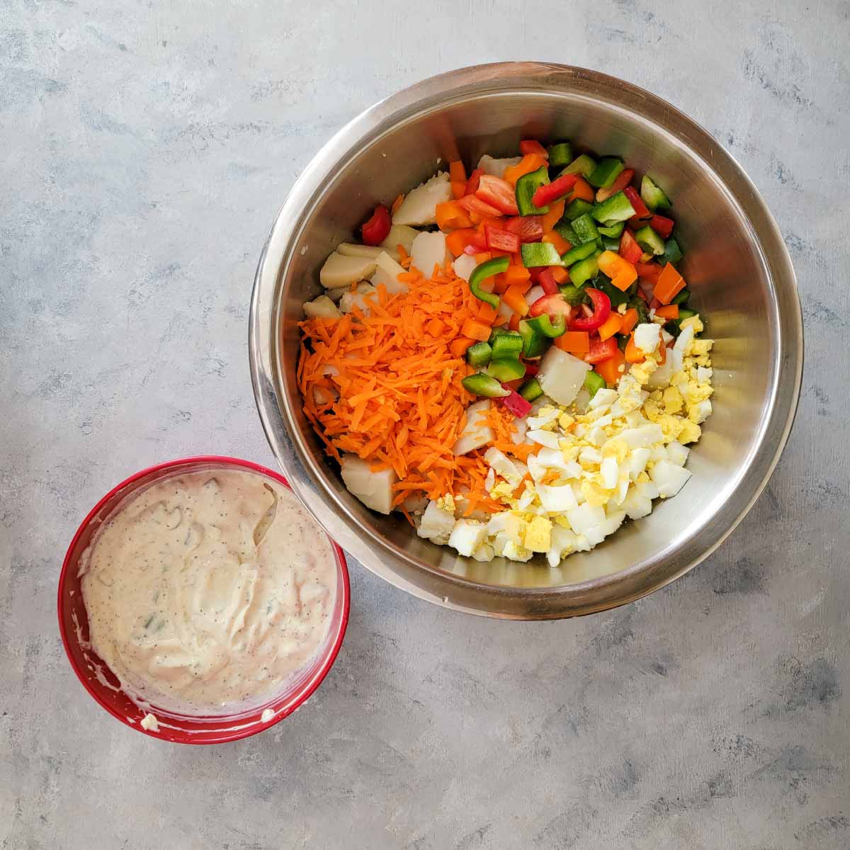 Cut potatoes, chopped peppers, chopped hard boiled eggs and shredded carrots in a large mixing bowl. The potato salad dressing is mixed already in a small prep bowl.
