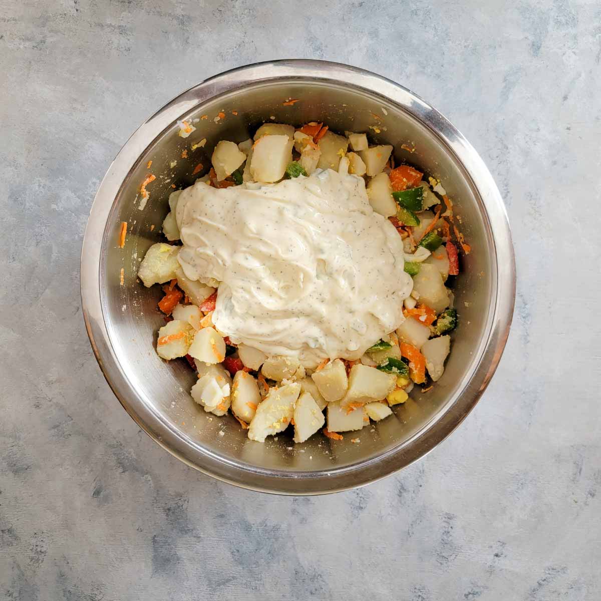 Potato chunks, peppers, chopped hard boiled eggs, carrots and the dressing in a large mixing bowl ready to stir.