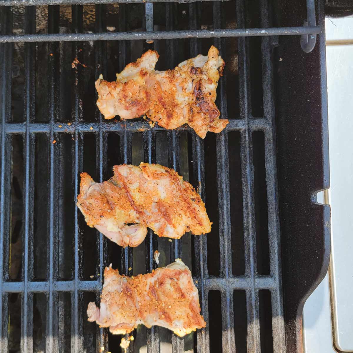 3 boneless chicken thighs on the grill after being flipped over with char marks on them.