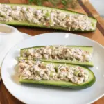 A cucumber cut in half with some of the inside scooped out. Dill tuna salad inside the center of the cucumber halves.