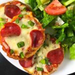 3 mini pizzas on a plate with a side of salad ready to serve.