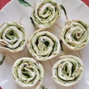 6 cucumber and cream cheese rolls on a serving plate ready to be served.