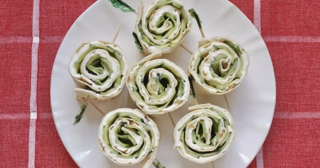 6 cucumber and cream cheese rolls on a serving plate ready to be served.