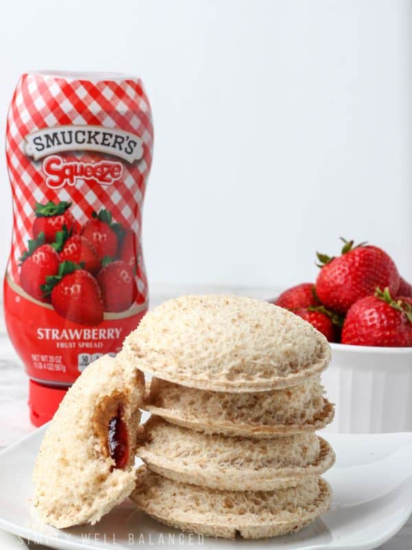4 homemade uncrustables stack on a plate with another leaning on them after a bite was taken out to show the peanut butter and jelly inside.