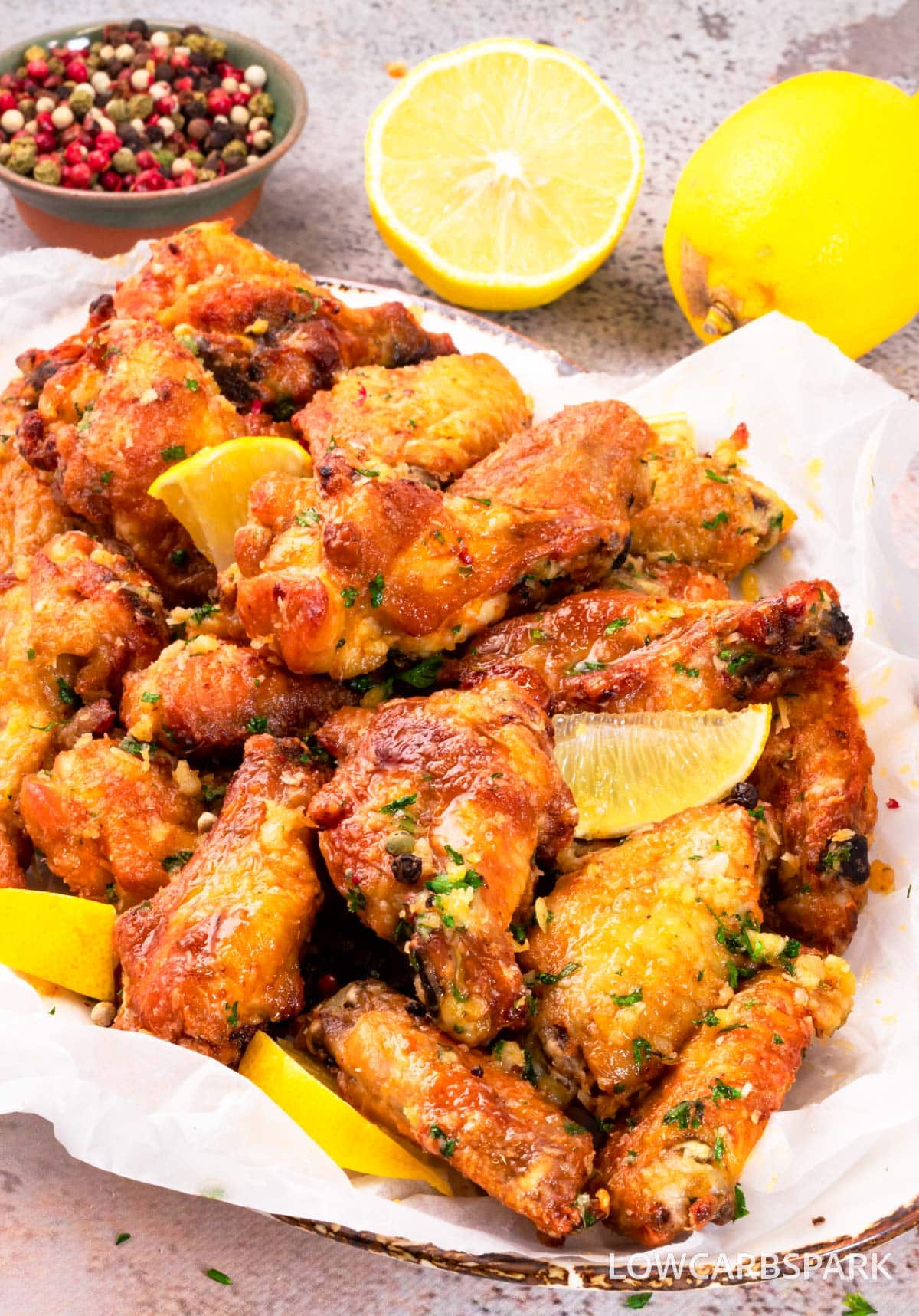 lemon pepper chicken wings in a serving dish with lemon slices served as a garnish.