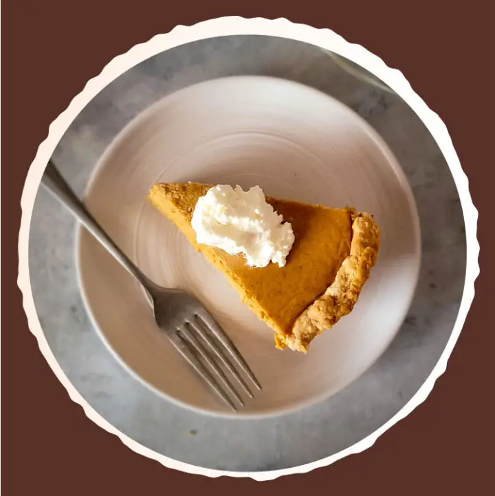 Slice of pumpkin pie on a plate topped with whipped cream.