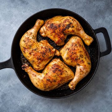 Leg quarters cooked to perfection with golden brown skin in a cast iron pan ready to serve.