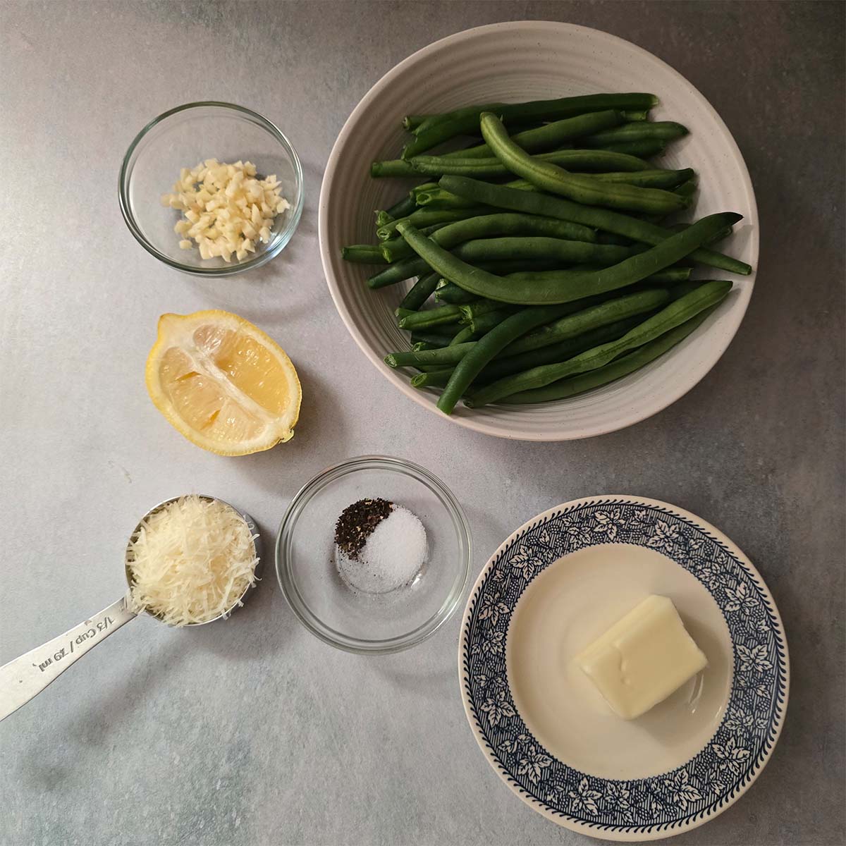 Image displaying the ingredients prepped - shredded parmesan, salt, pepper, butter, half a lemon and the green beans.