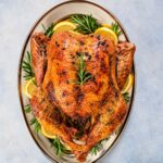Golden-brown lemon rosemary roast turkey with garlic and butter, served with fresh lemon and rosemary.