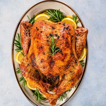 Golden-brown lemon rosemary roast turkey with garlic and butter, served with fresh lemon and rosemary.
